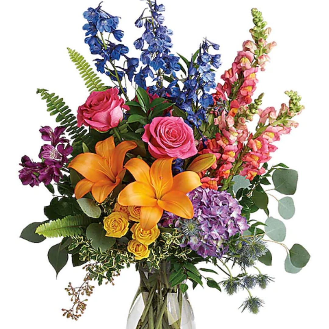 Colorful mixed bouquet in a clear glass vase with lilies, roses, and tall blue blooms