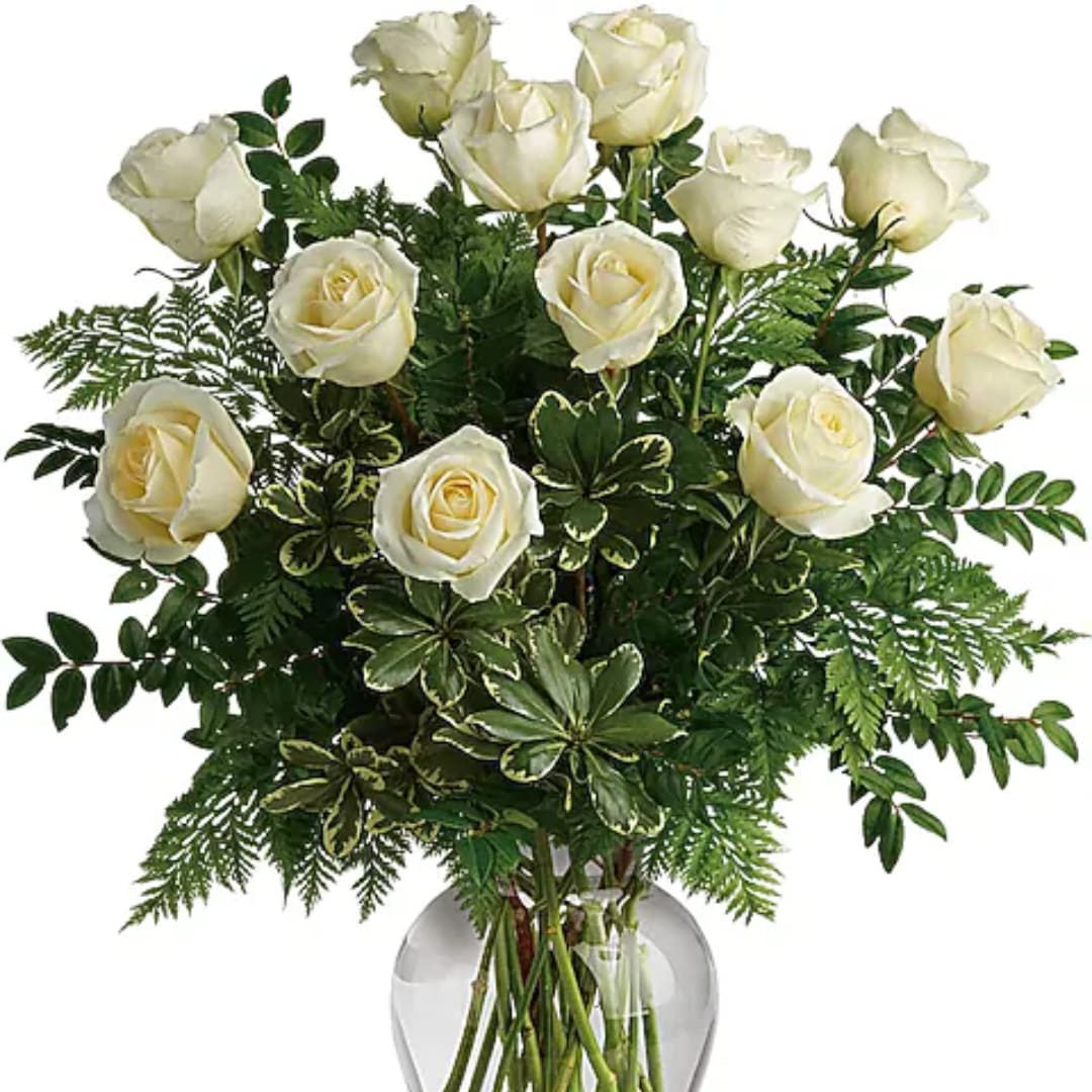 White roses arranged in a clear glass vase with dense greenery