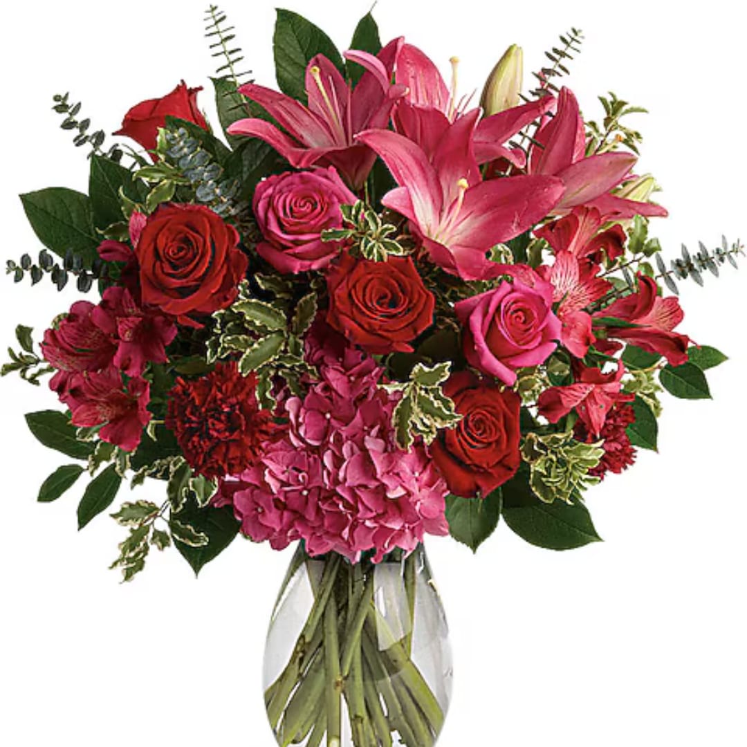 Bouquet of pink lilies, red roses, and pink hydrangeas in a glass vase