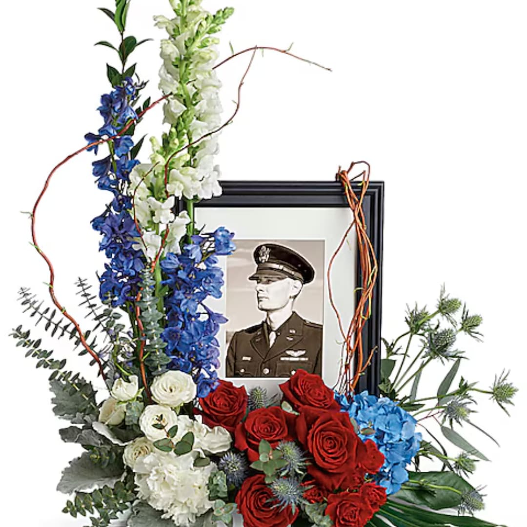 Floral tribute with red and white roses around a framed military portrait