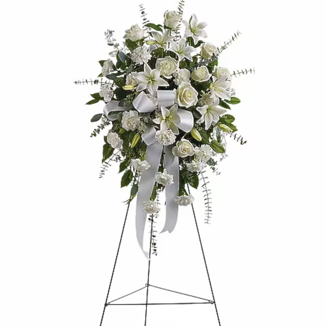 White floral standing spray with lilies, roses, and ribbon on an easel