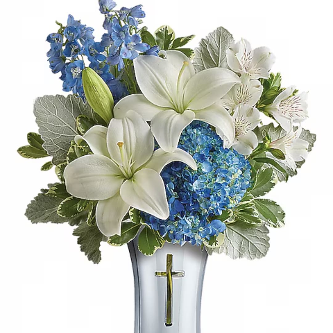 White lilies and blue flowers arranged in a clear vase with a cross