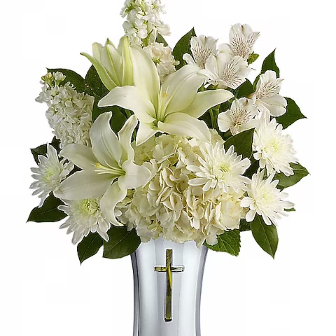 White lilies and daisies arranged in a clear vase with a cross emblem
