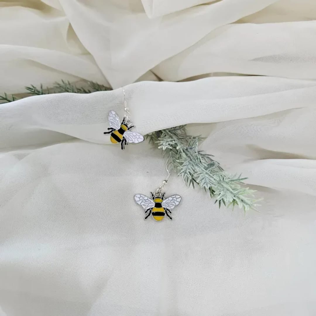 White fabric with two bee-shaped dangling earrings and faux greenery