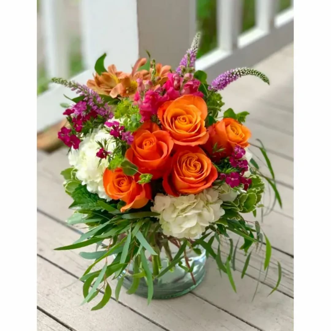 Bright mixed bouquet of orange roses, white hydrangea, and pink accents in a glass vase