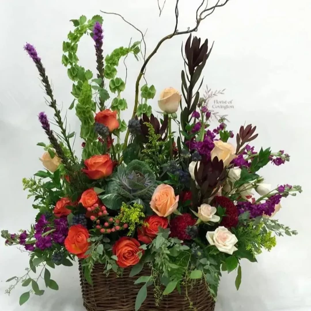Large mixed flower arrangement in a wicker basket with orange, cream, and purple blooms