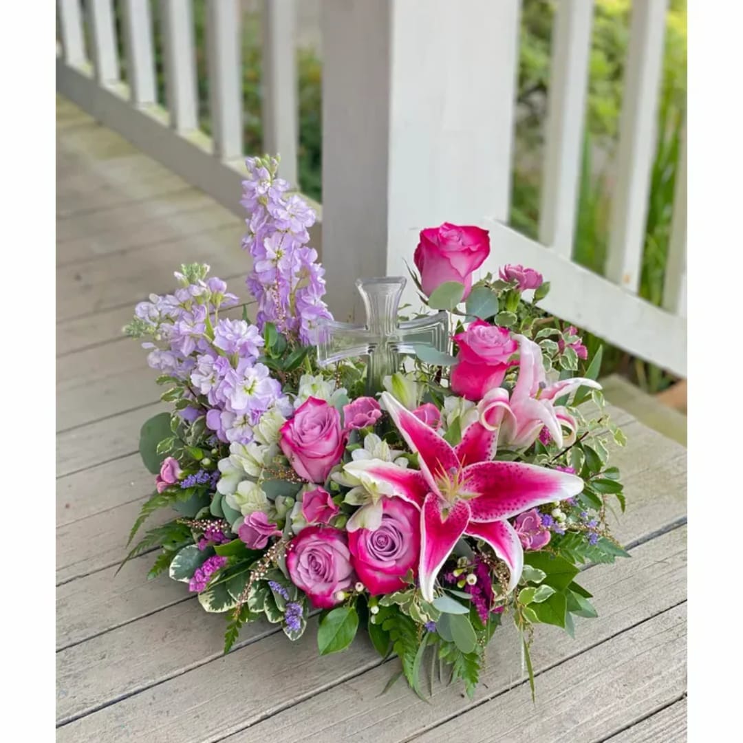 Pink and lavender floral arrangement with roses and lilies in a clear cross vase