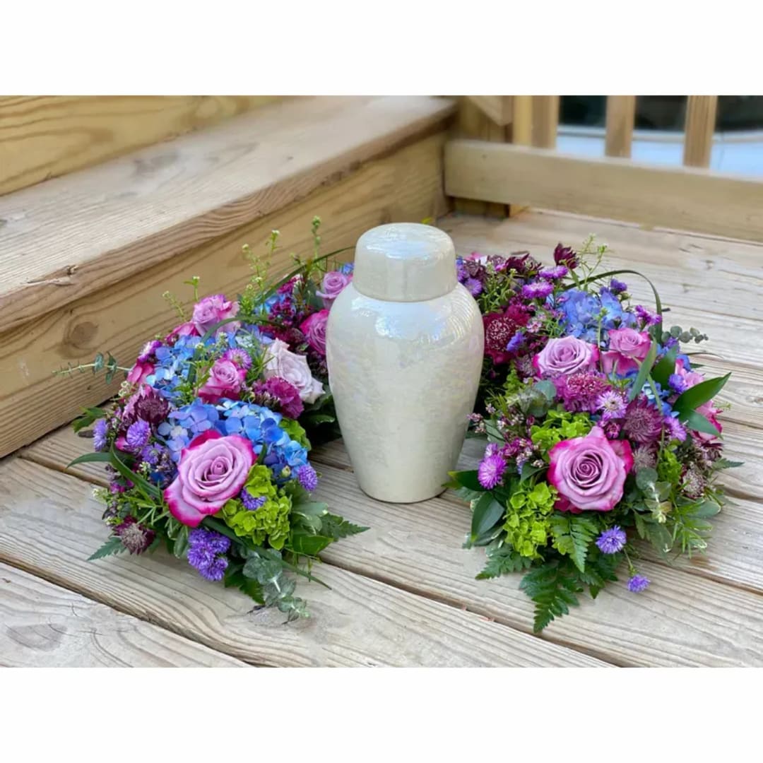Floral wreath with pink roses and purple-blue blooms around a white urn
