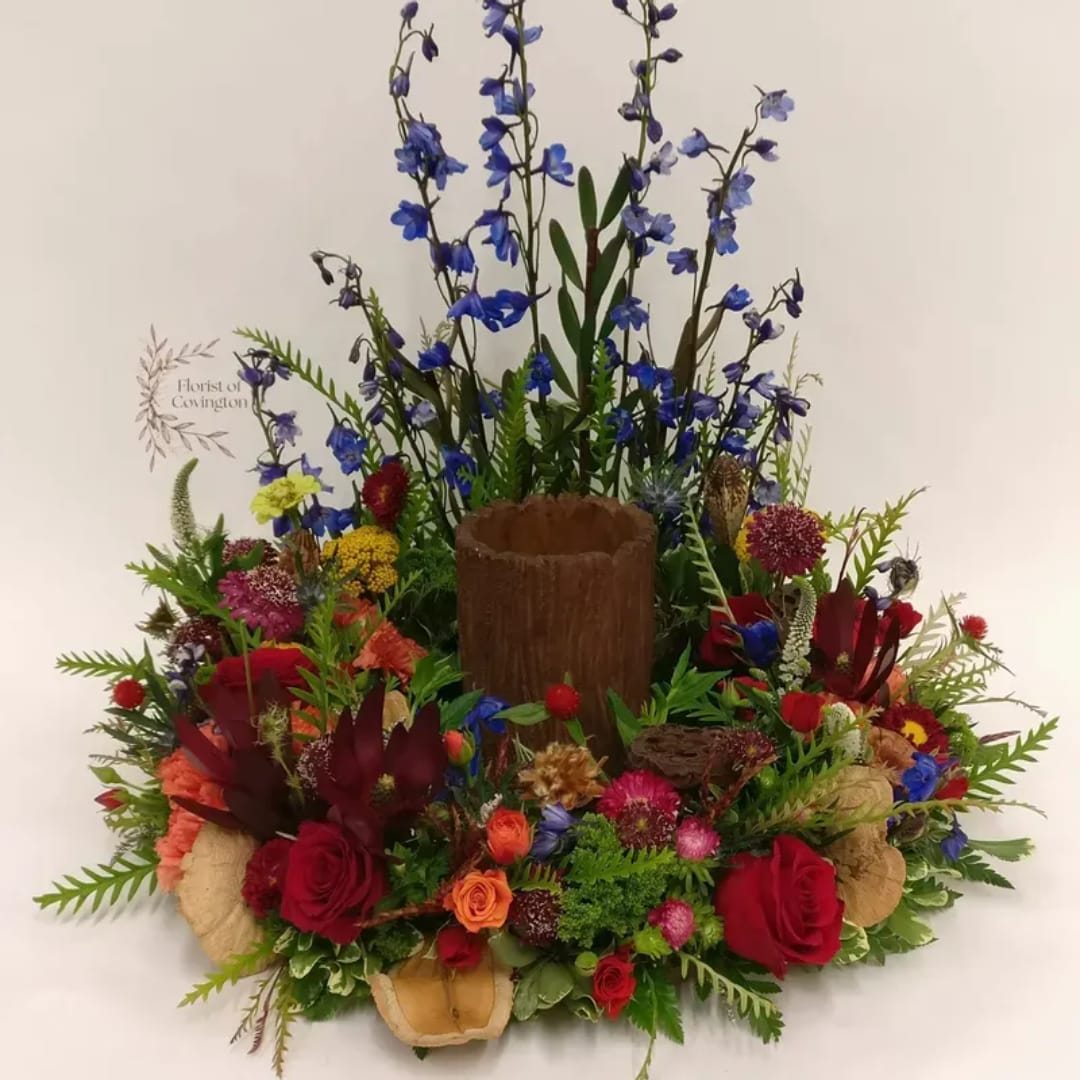 Colorful floral arrangement with red roses and tall blue flowers in a wooden container