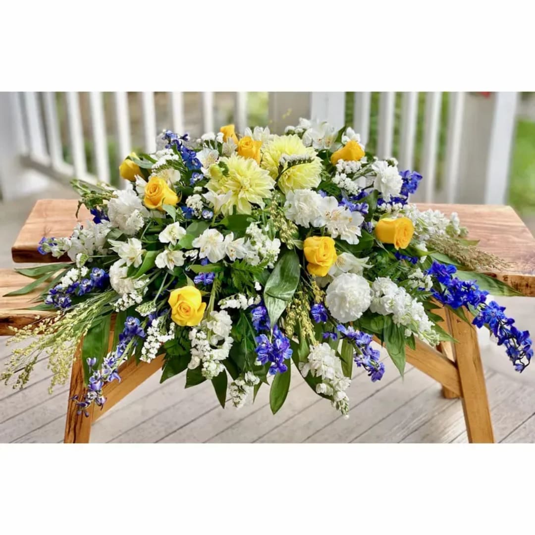 Large floral arrangement with yellow roses, white blooms, and blue flowers on a wooden table