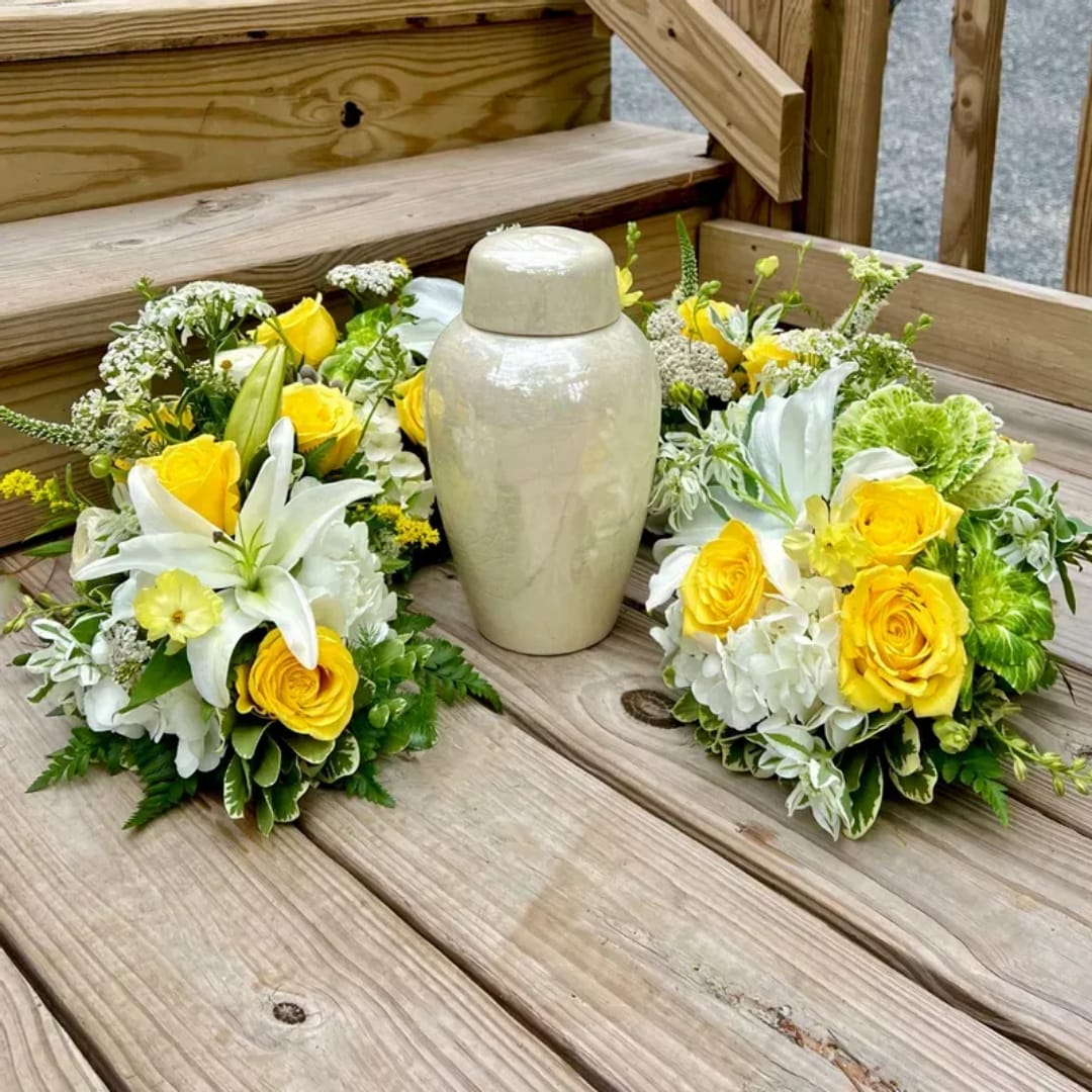 Yellow and white floral arrangements around a cream urn on a wooden deck