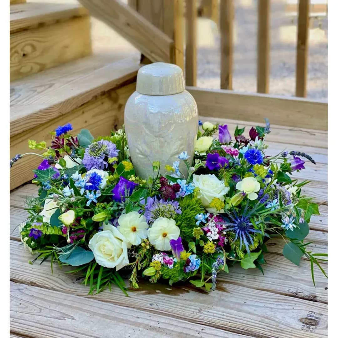 Low floral wreath around a white urn on a wooden deck
