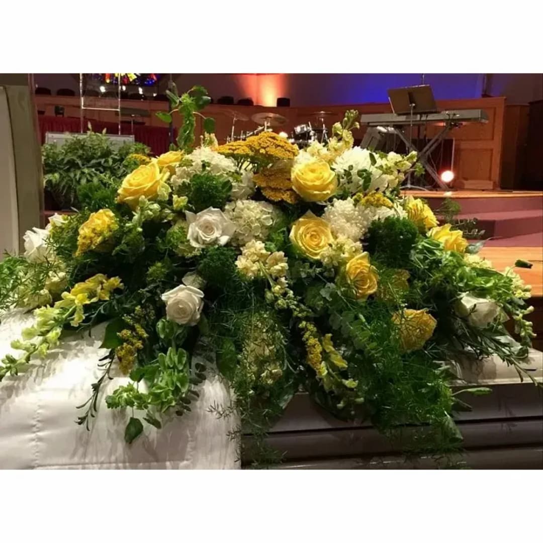 Large yellow and white floral arrangement on a casket
