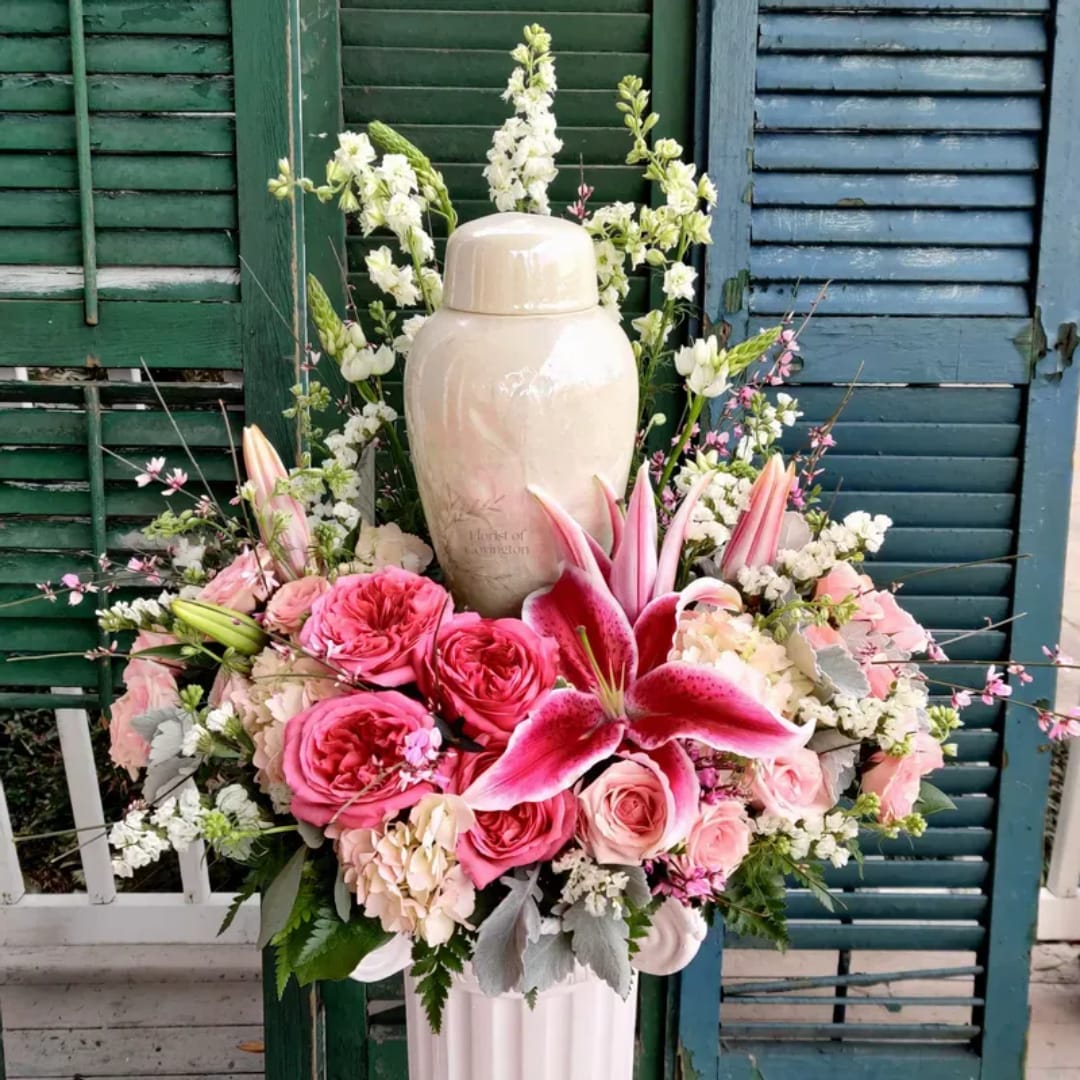 Pink and white floral arrangement around a beige urn on a pedestal