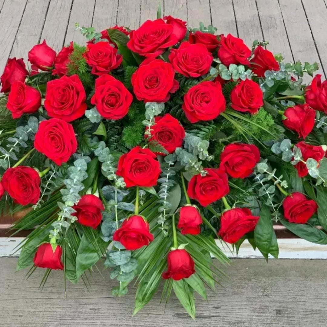 Large arrangement of red roses with mixed greenery on a wooden surface