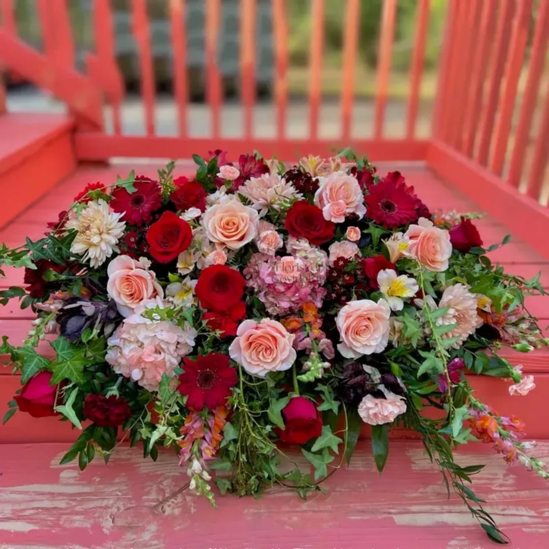 Mixed bouquet of red and blush roses with assorted flowers on a pink bench