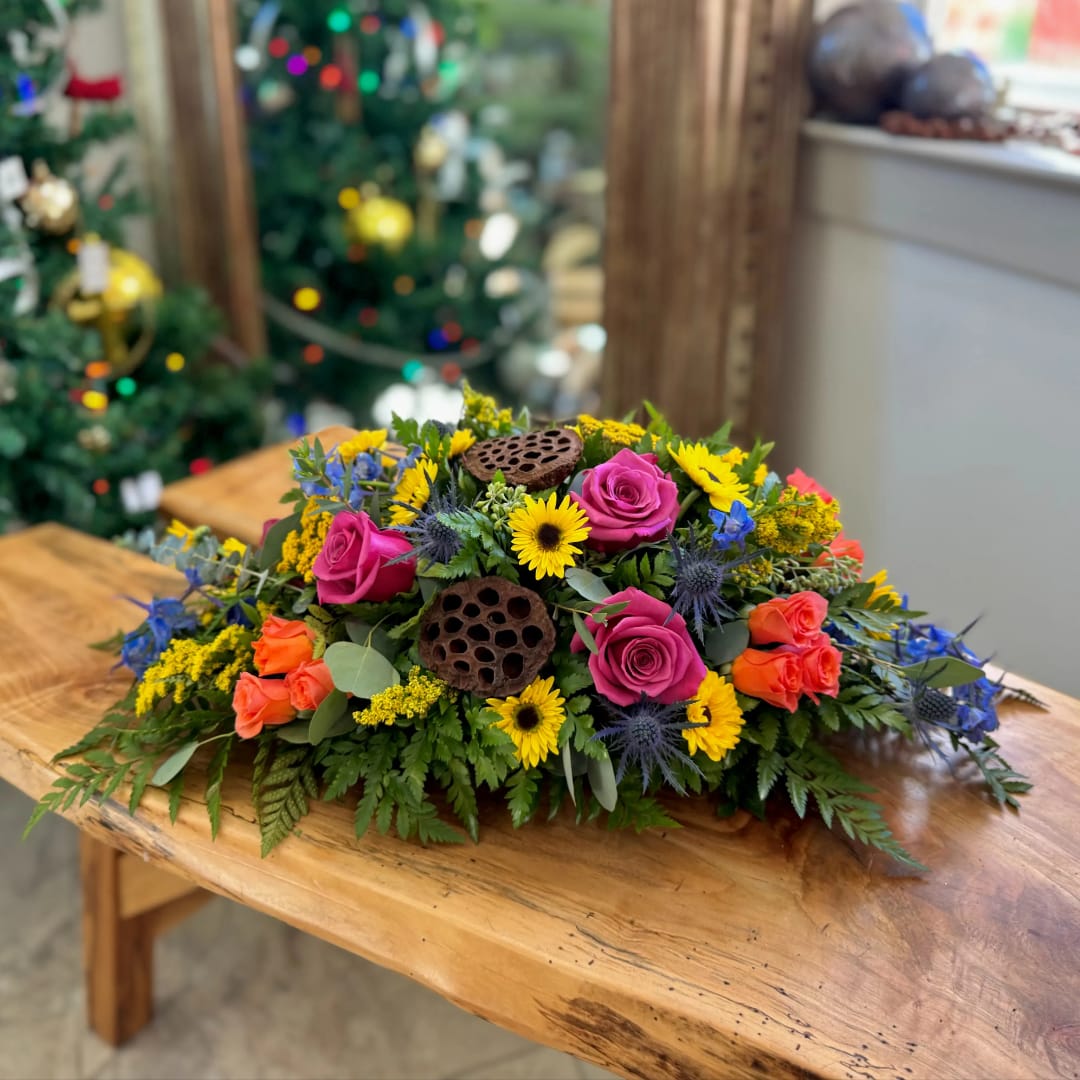 Low floral centerpiece with pink roses, yellow daisies, and blue accents