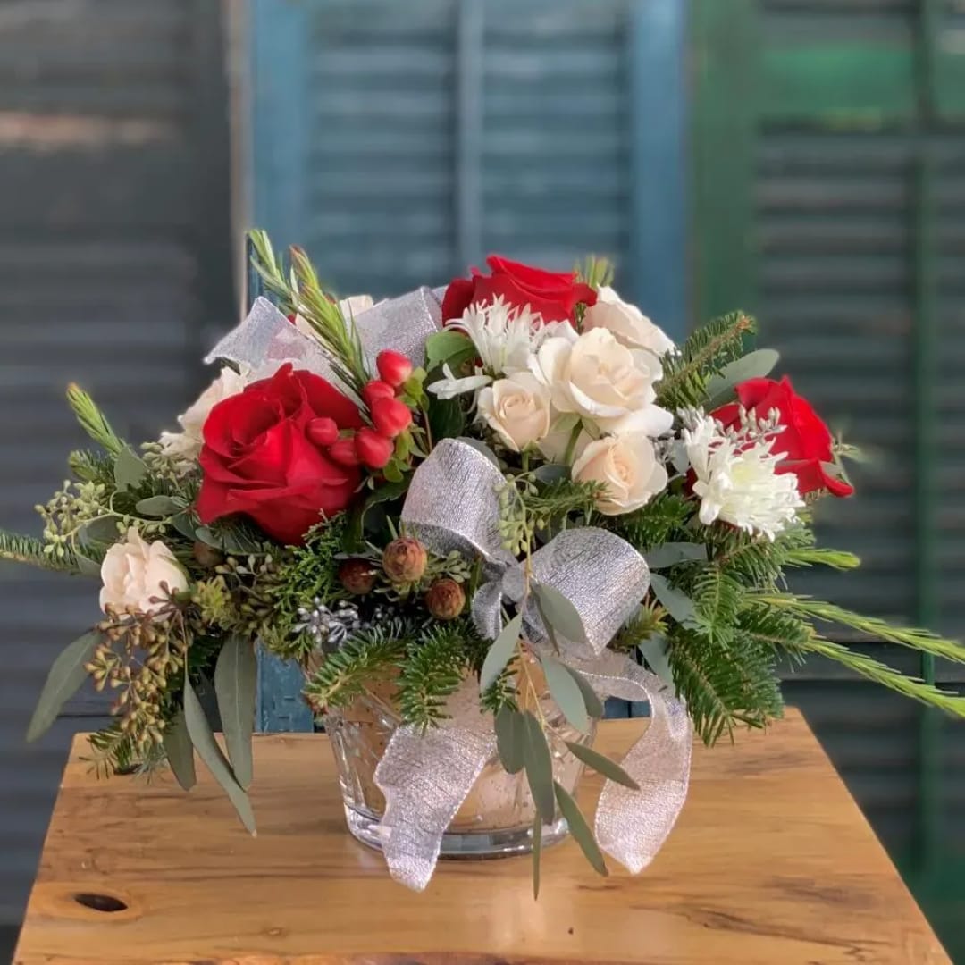 Red and white roses arranged in a glass vase with a silver ribbon