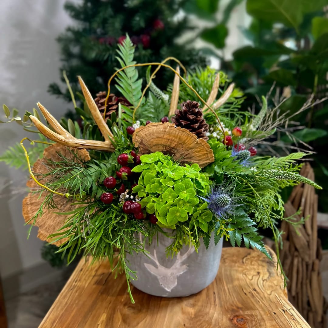 Green floral arrangement in a gray vase with pinecones and dried accents