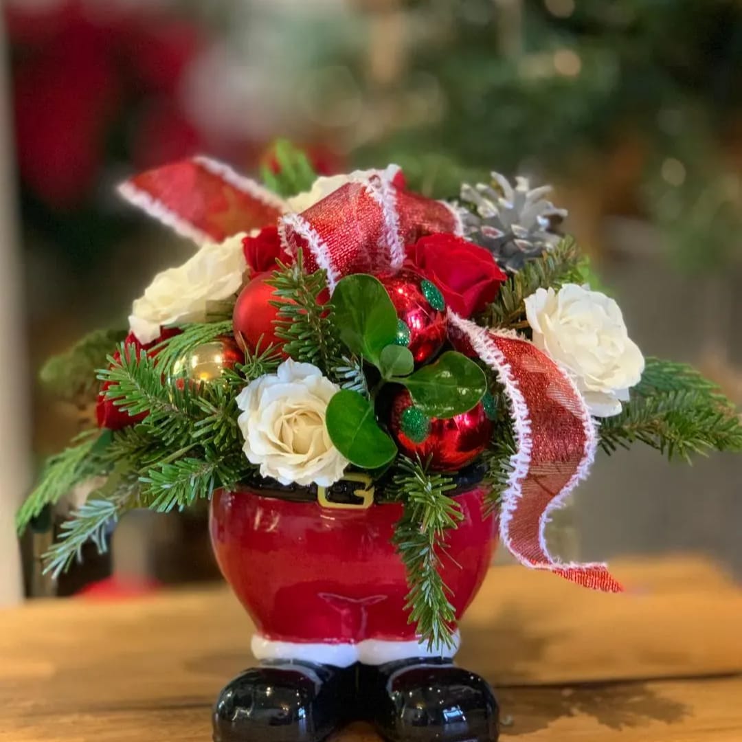 Christmas floral arrangement in a red Santa-shaped container with roses and ribbon