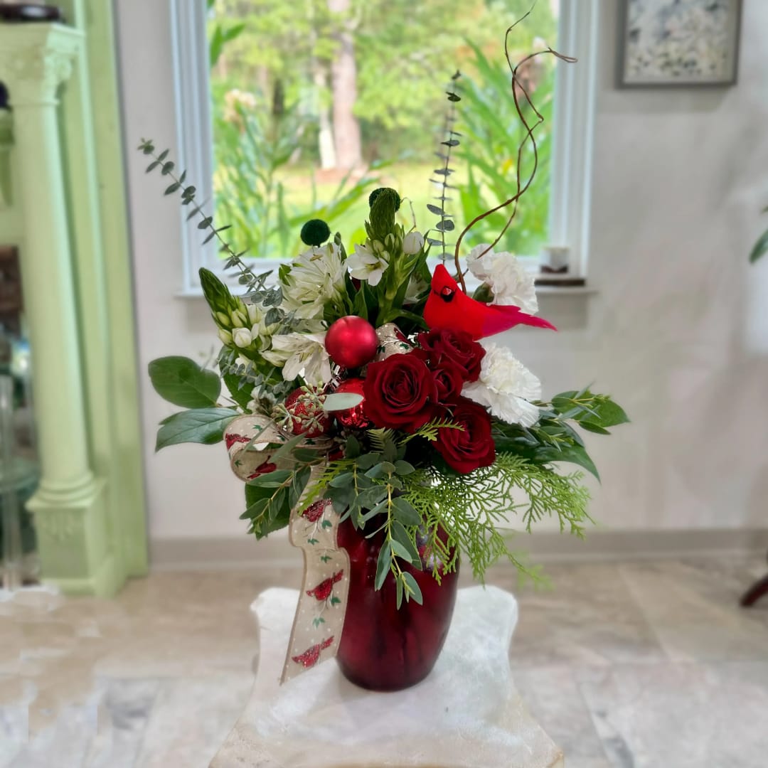 Red roses and white flowers arranged in a burgundy vase with holiday ribbon.