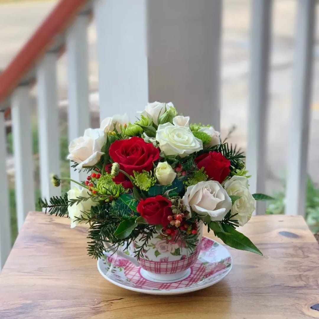 Red and white roses arranged in a floral teacup on a saucer
