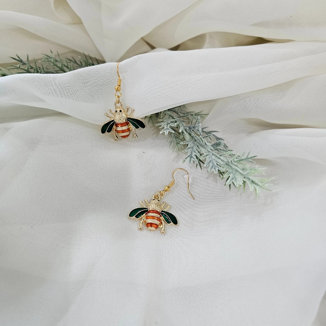 Pair of bee-shaped drop earrings on white fabric with faux greenery