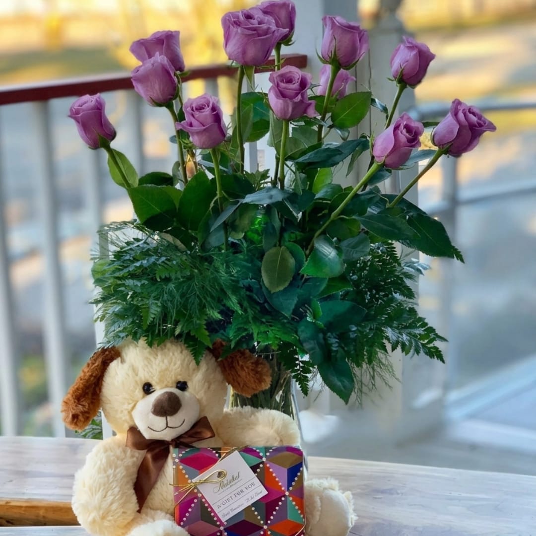 Purple roses in a glass vase with a teddy bear and gift box