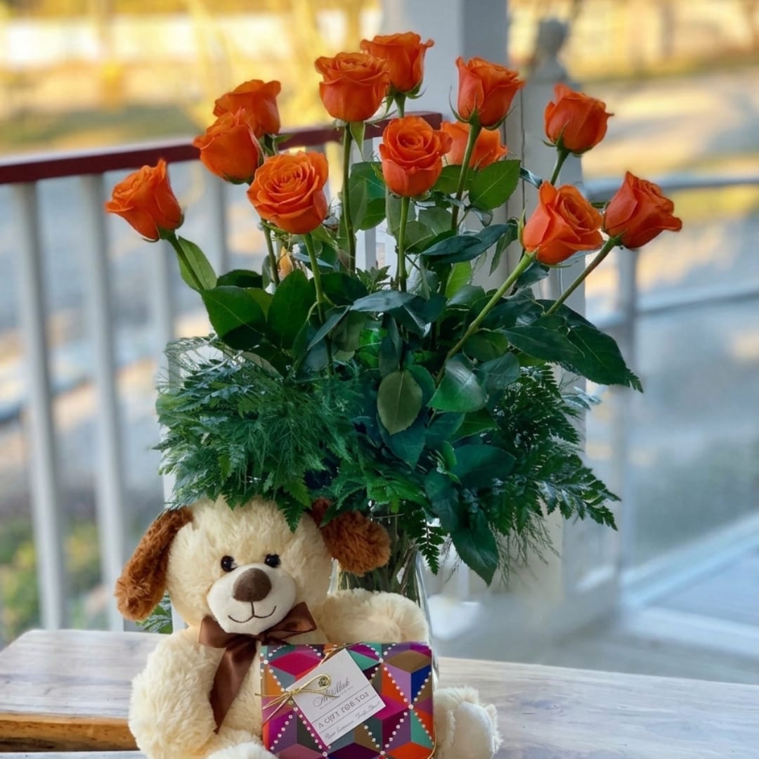 Orange roses in a glass vase with a teddy bear and gift box