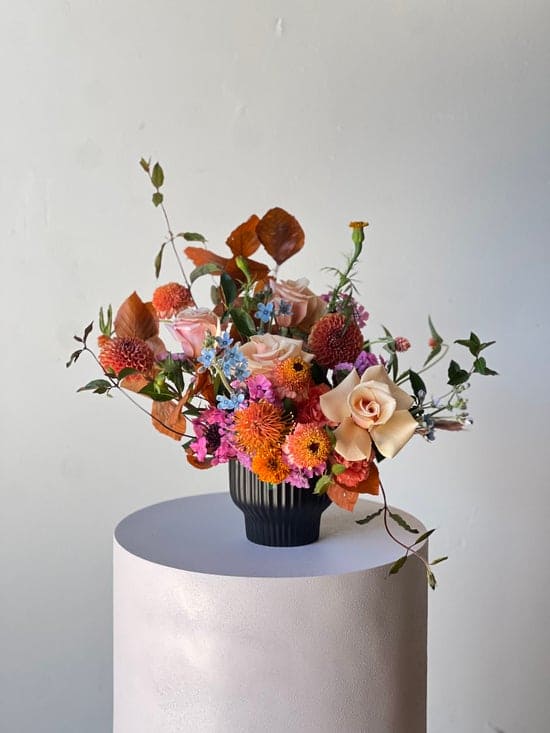 Mixed bouquet of orange, pink, and cream flowers in a black vase