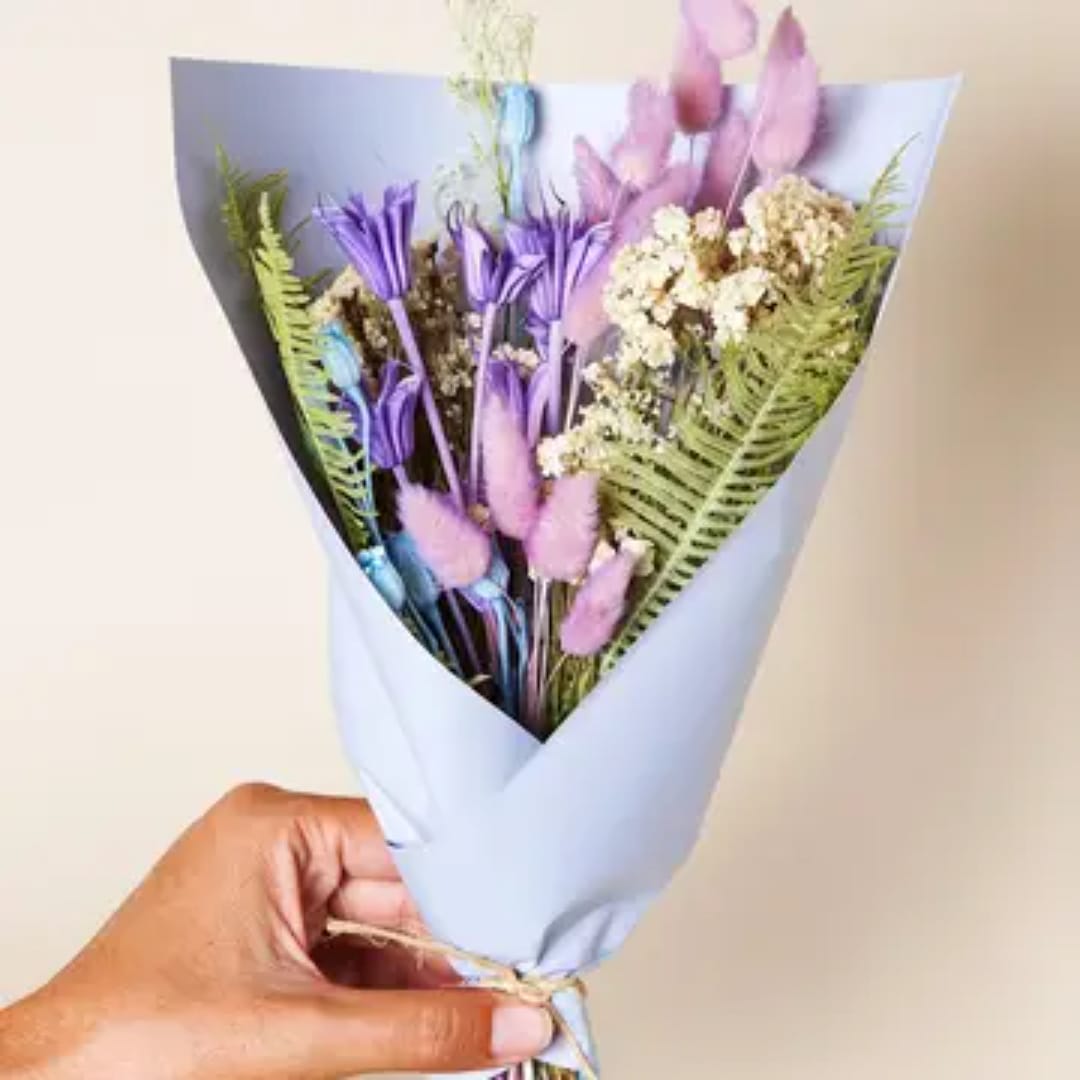 Handheld bouquet of purple and pink flowers wrapped in pale blue paper