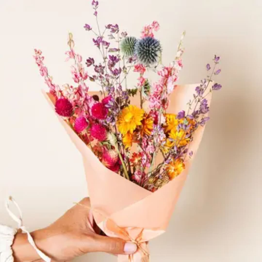 Handheld bouquet of colorful dried flowers wrapped in peach paper