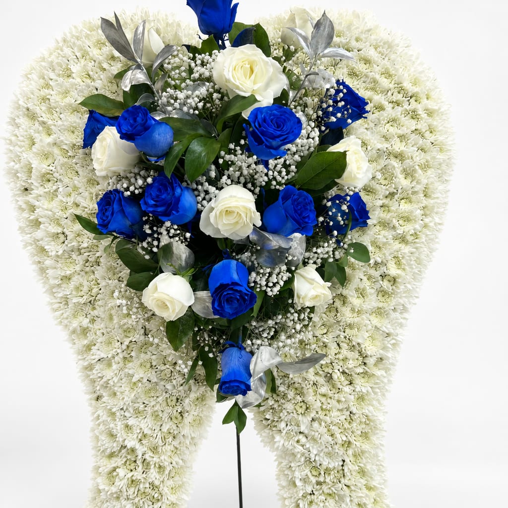 Heart-shaped funeral spray with blue and white roses on a white chrysanthemum base