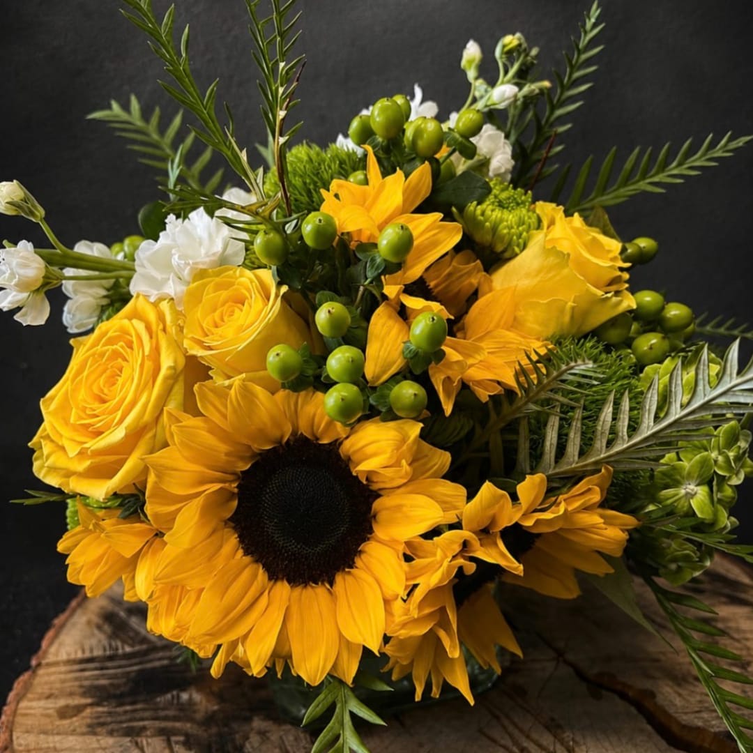 Yellow sunflowers and roses arranged with white blooms and green berries
