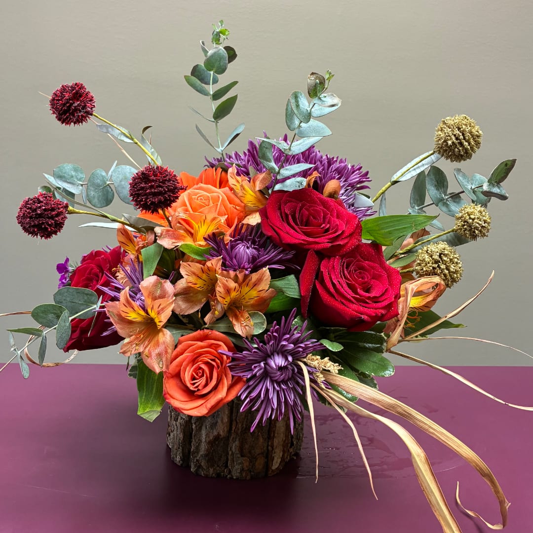Mixed bouquet of red, orange, and purple flowers in a rustic vase