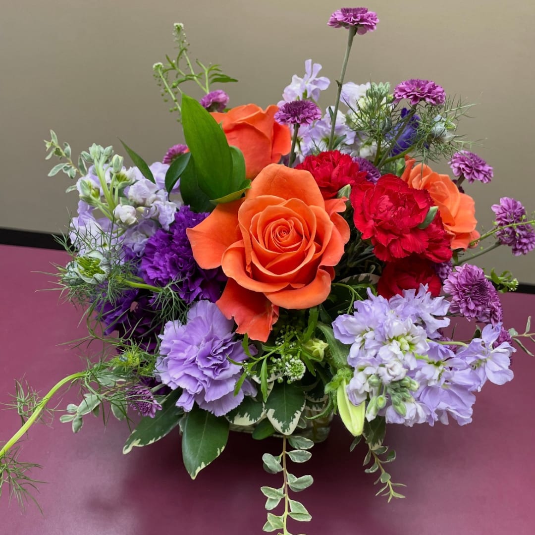 Orange roses and purple flowers in a low bouquet