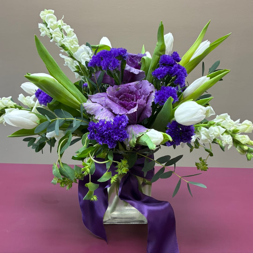 Purple and white floral arrangement in a square vase with ribbon