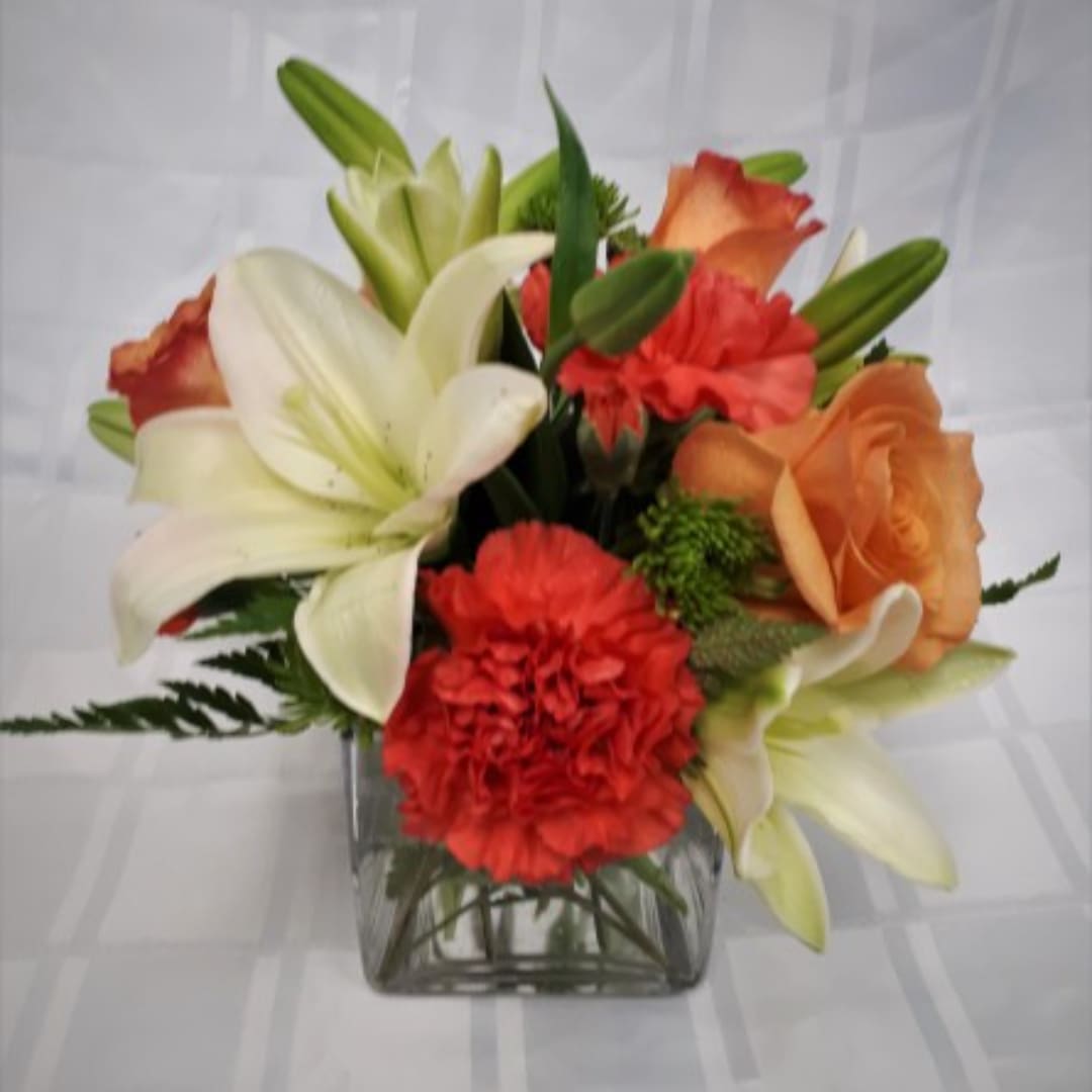 Autumn Special Bouquet - An elegant selection of flowers placed in a clear glass cube vase. This all around design in orange and white included lilies, carnations, roses and more. Product ID Fall20193D Approximately 7"W x 8"H