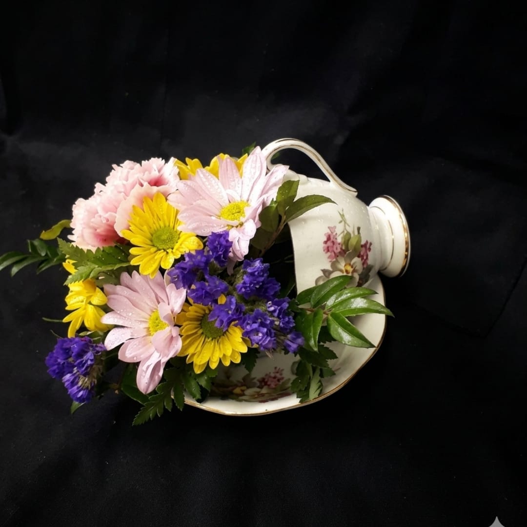 Mixed pink, yellow, and purple flowers arranged in a floral teacup