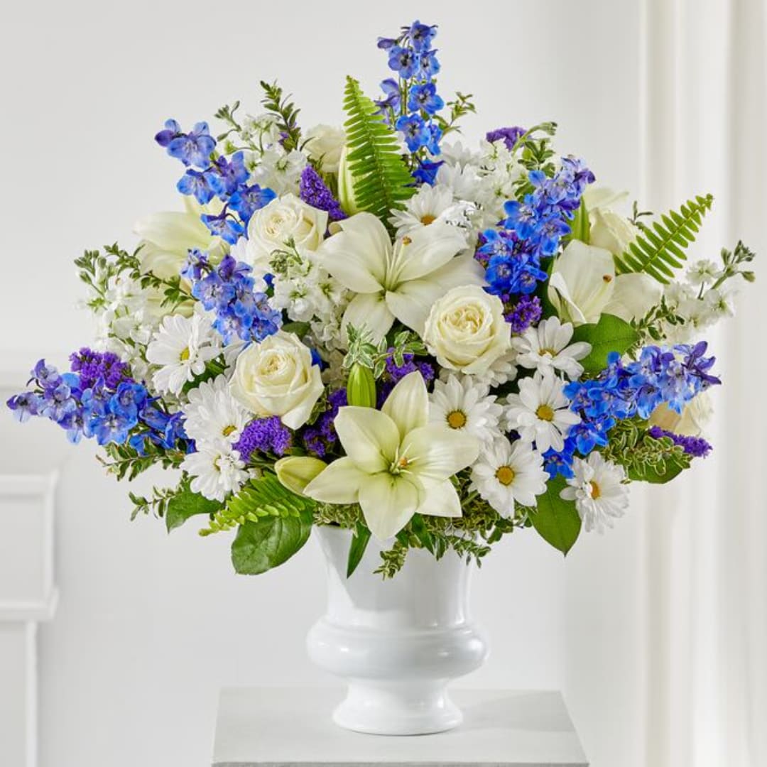 White and blue mixed flower arrangement in a white pedestal vase