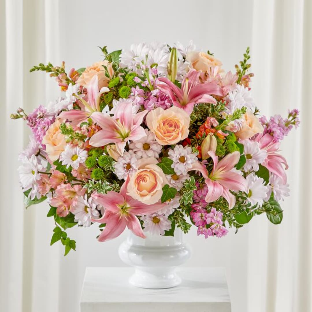 Pink lilies, peach roses, and white daisies in a white pedestal vase
