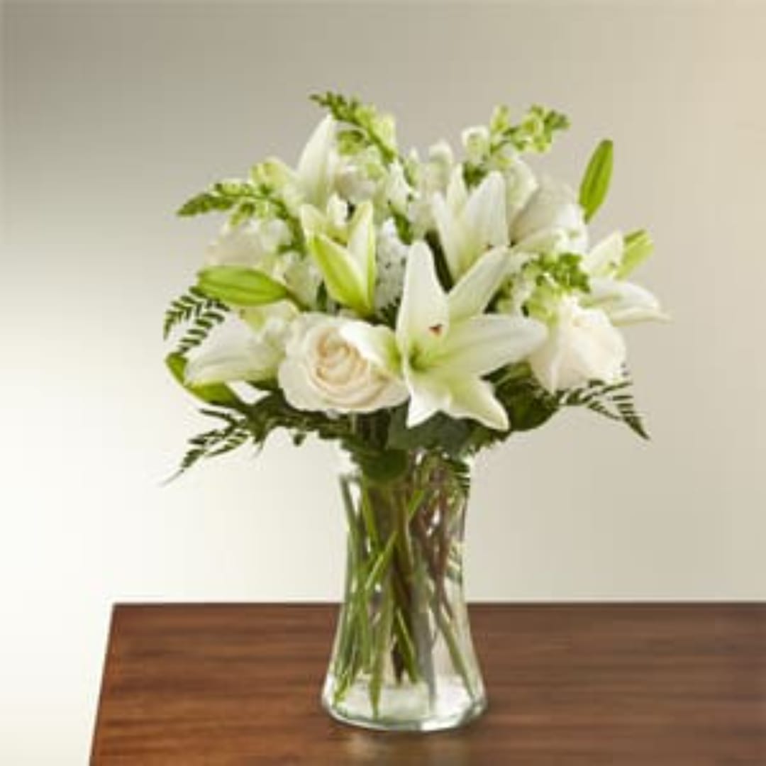 White lilies and roses arranged in a clear glass vase