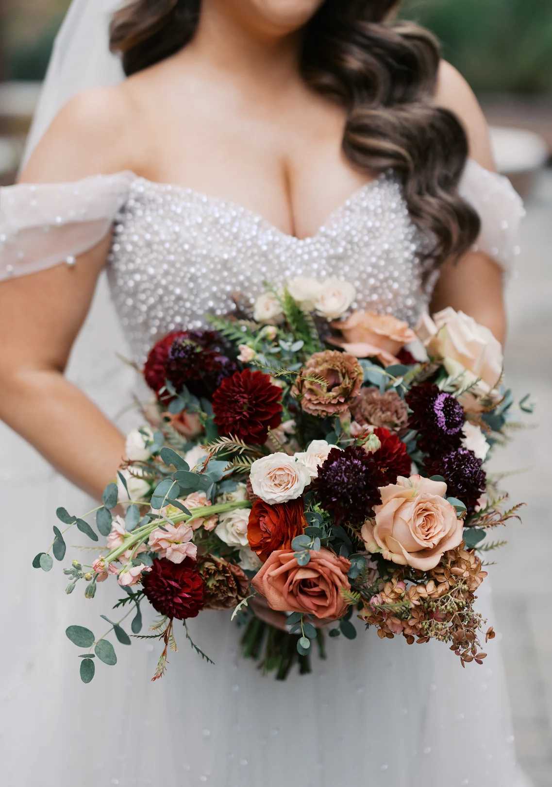 Bride holding a bouquet of blush, burgundy, and peach flowers
