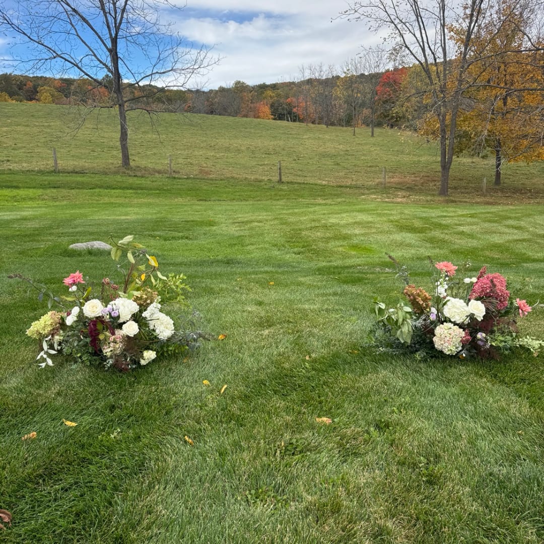 Two low floral arrangements on grass in an open field