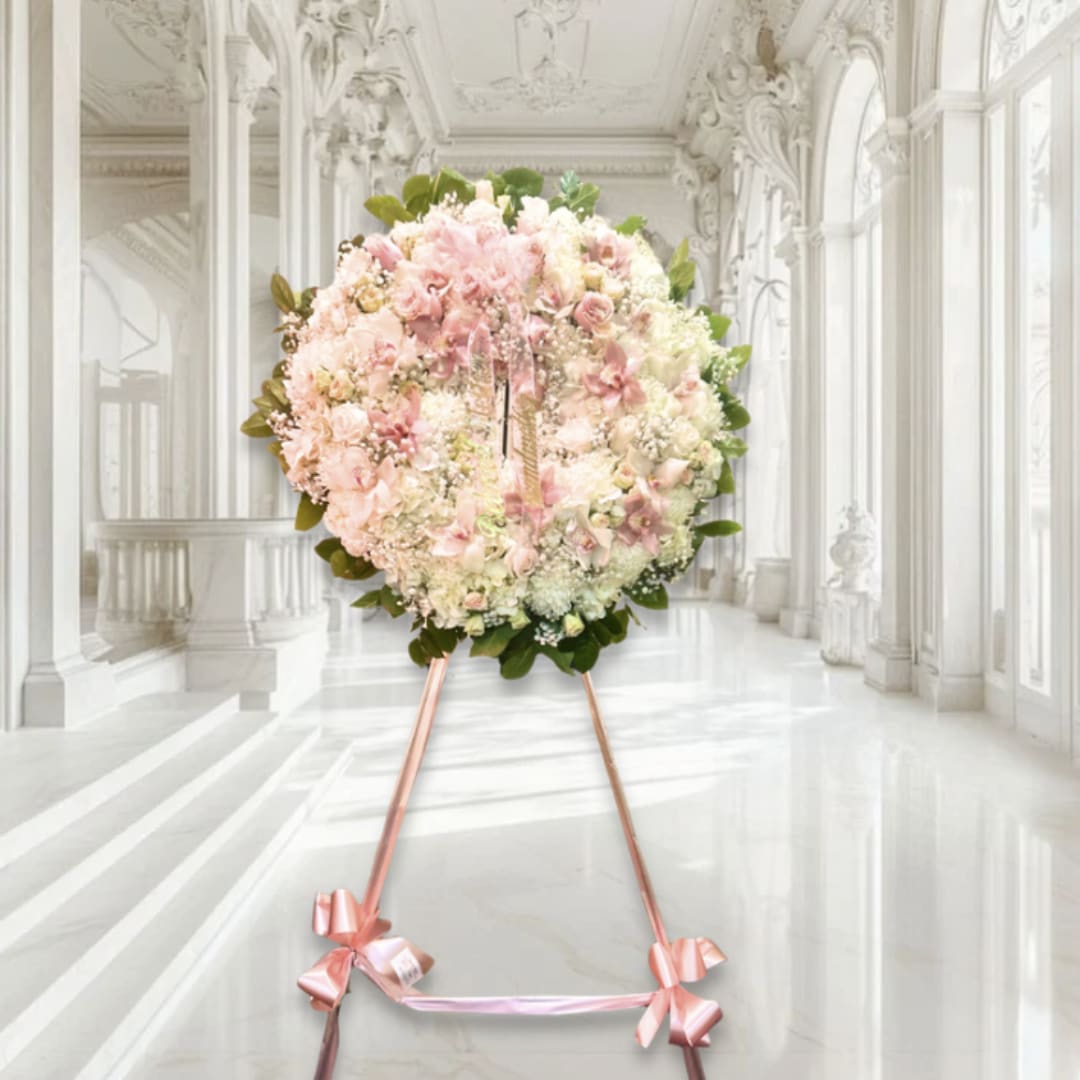 Large pink and white floral wreath on a stand with ribbon bows