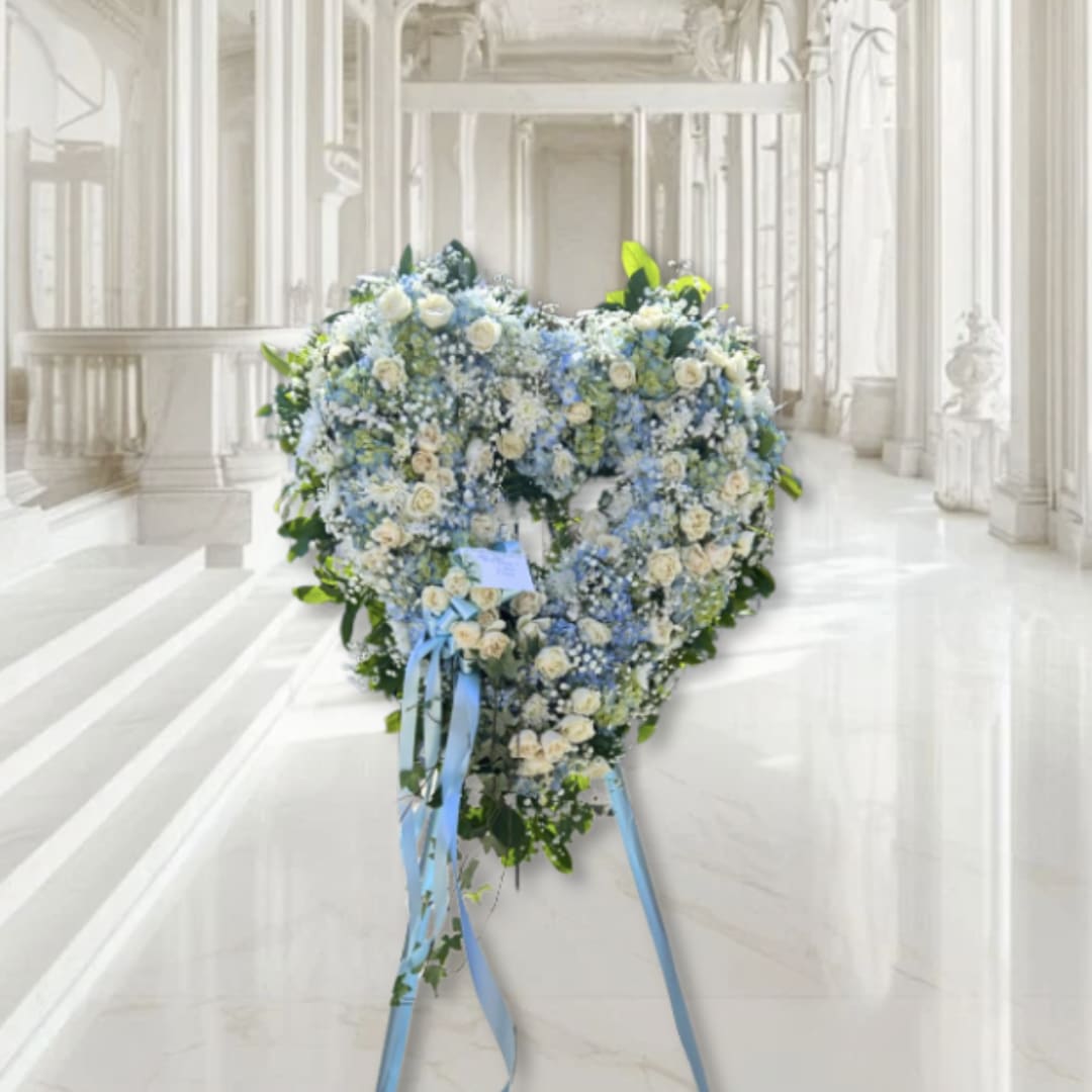 Heart-shaped floral wreath with white and blue flowers on a stand