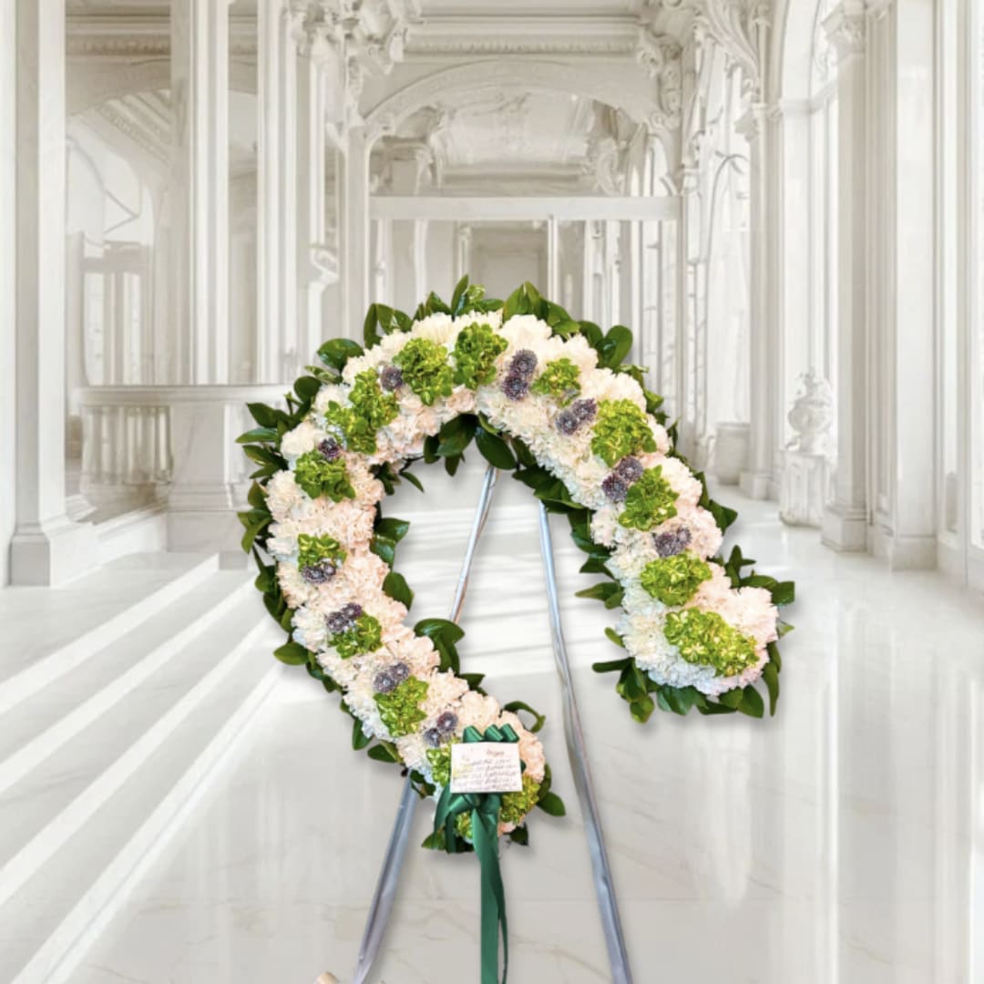White and green floral funeral wreath on a stand with a ribbon