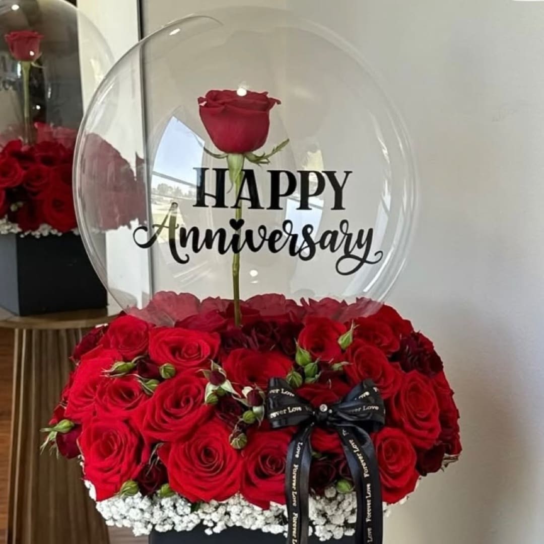Red rose arrangement in a clear balloon with "Happy Anniversary" text