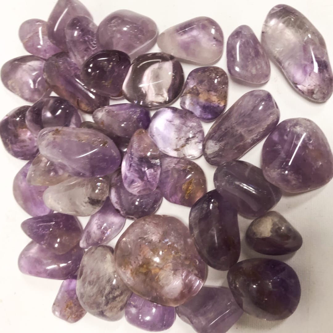Pile of polished purple amethyst stones on a white surface