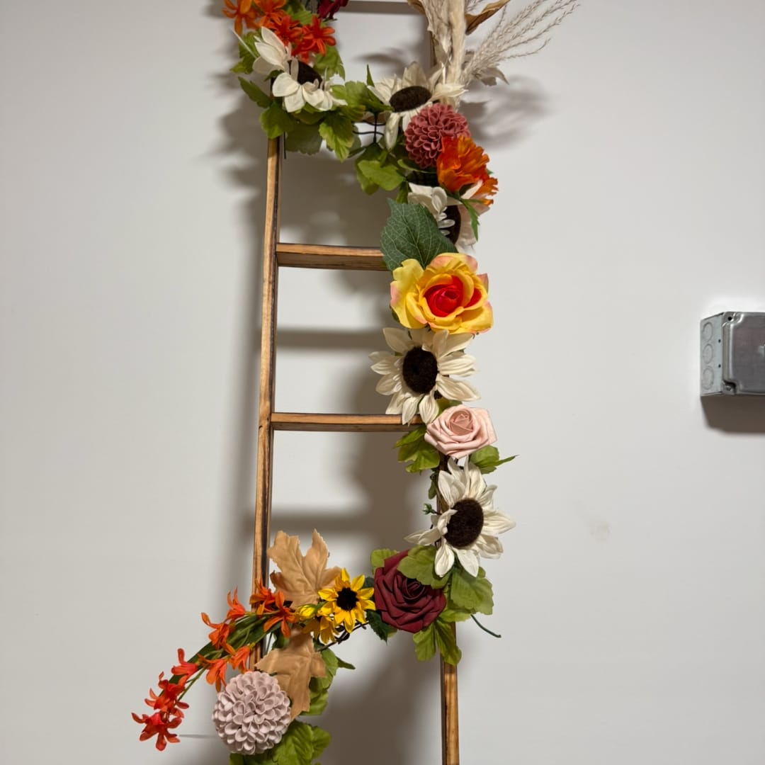 Floral garland with mixed blooms draped on a wooden ladder